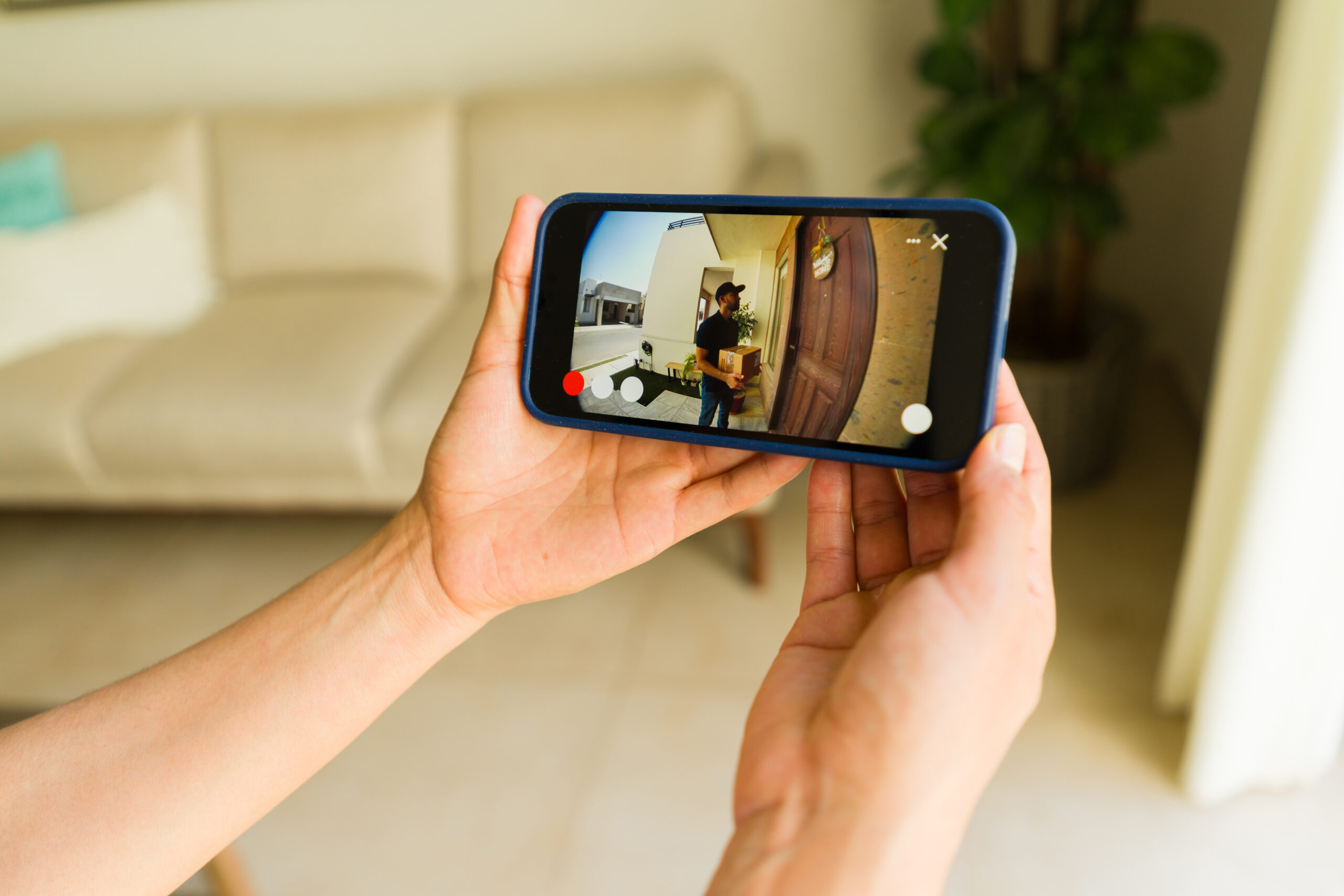 Closeup of a woman using a smartphone app to watch a delivery man dropping off a package