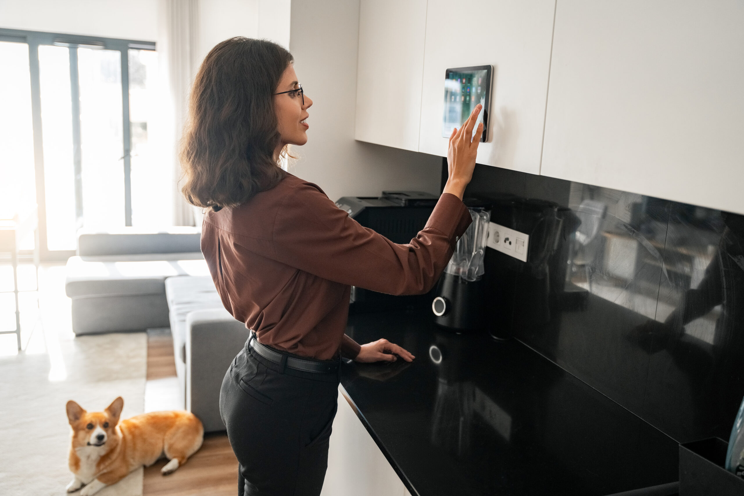 Smiling young woman using screen device gadget for remote control for air conditioning, cleaning housekeeping, touching tablet computer on wall. Beautiful lady enjoy of new intelligence technologies.